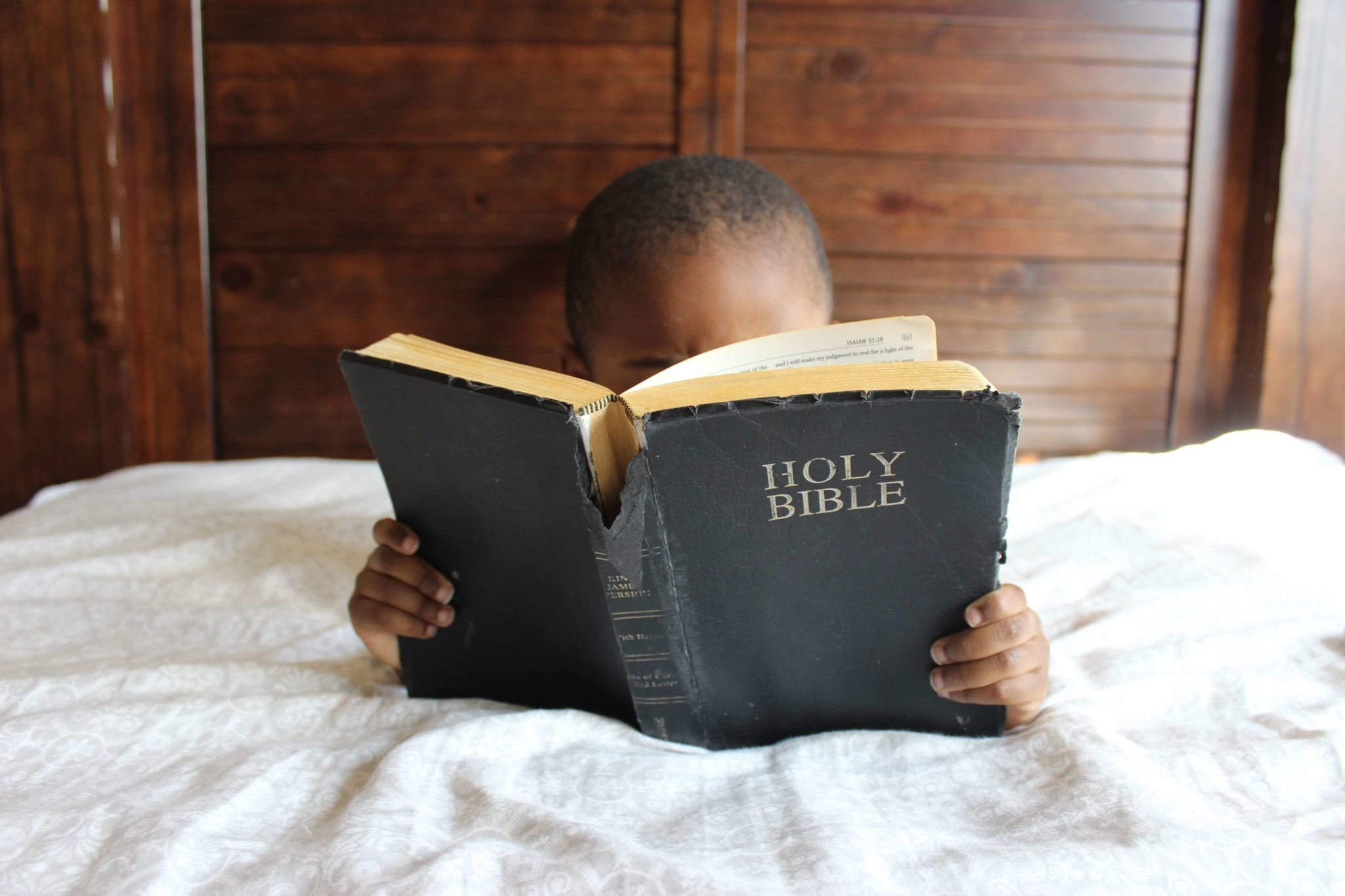 A picture of a young child reading the bible. learn how to reduce social media use and replace with bible reading.